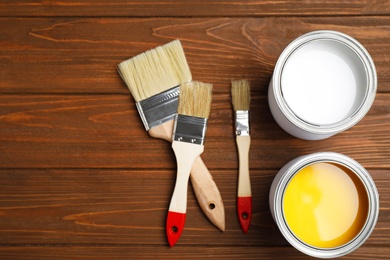 Open cans with paint and brushes on wooden table, flat lay