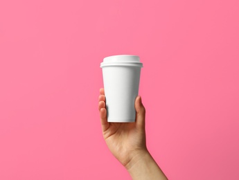 Photo of Woman holding takeaway paper coffee cup on pink background, closeup