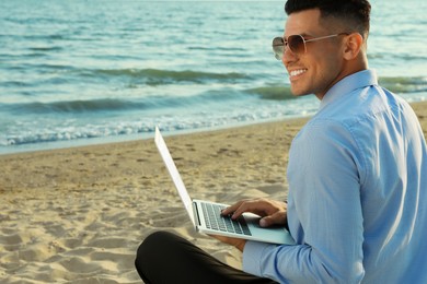 Photo of Happy businessman working with laptop on beach. Business trip