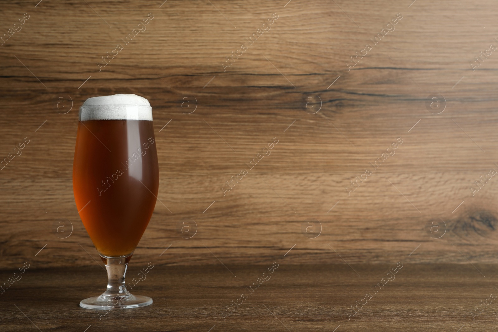 Photo of Glass of tasty beer on wooden table. Space for text