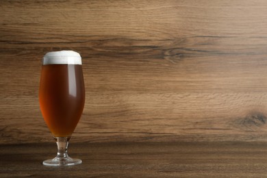 Photo of Glass of tasty beer on wooden table. Space for text