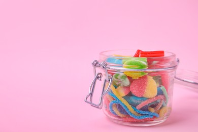 Tasty jelly candies in open jar on pink background, closeup. Space for text