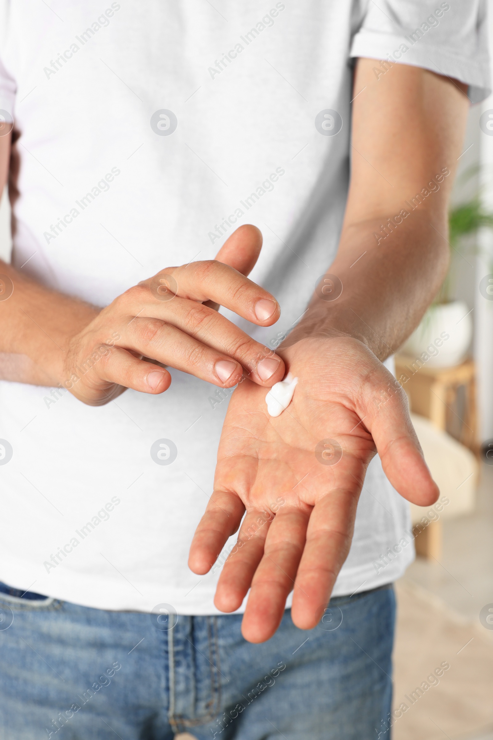 Photo of Man applying cream onto hand indoors, closeup