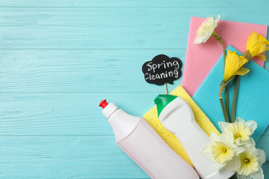 Photo of Composition with Spring Cleaning sign, flowers and detergents on light blue wooden table, flat lay. Space for text