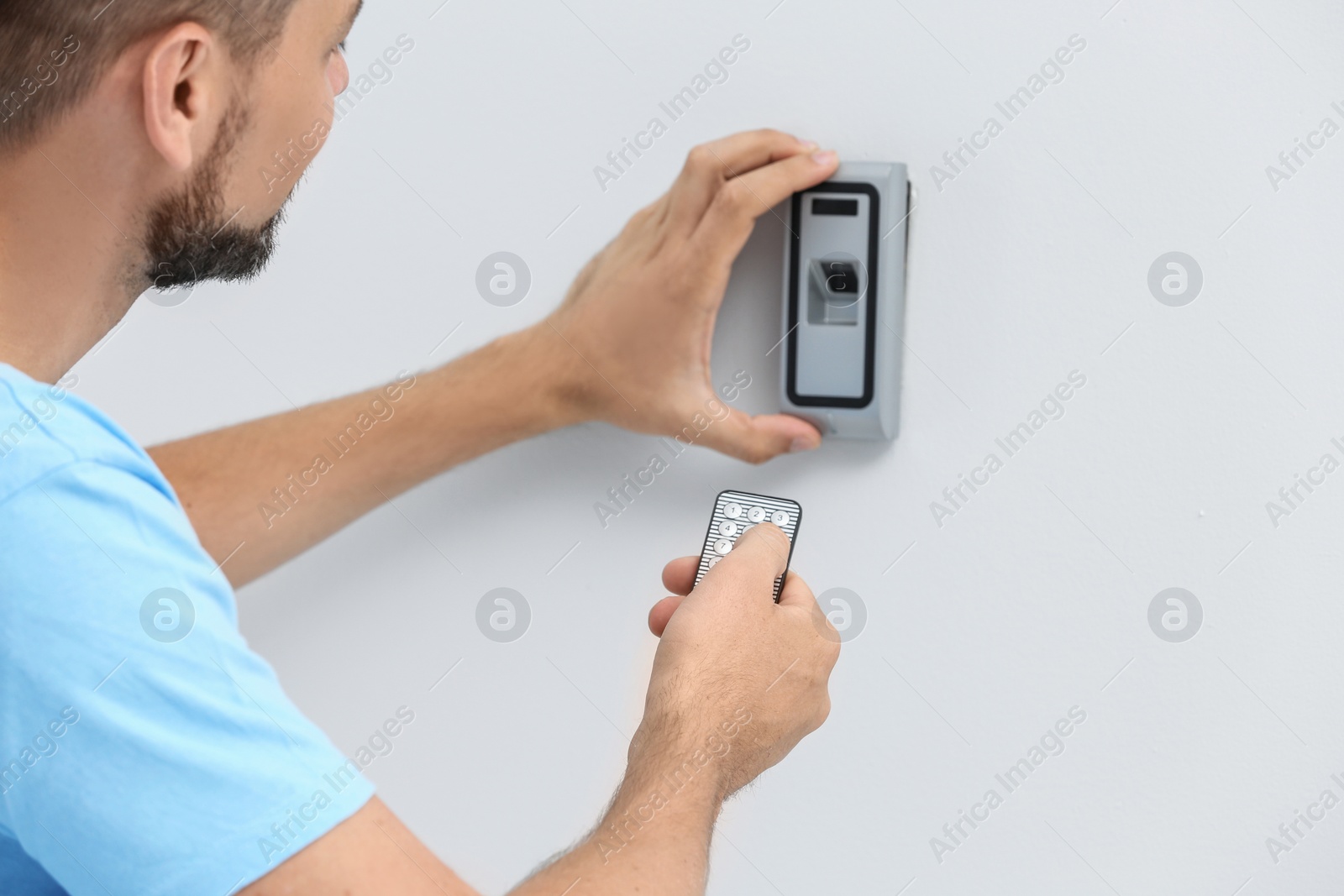 Photo of Young male technician programming alarm system indoors