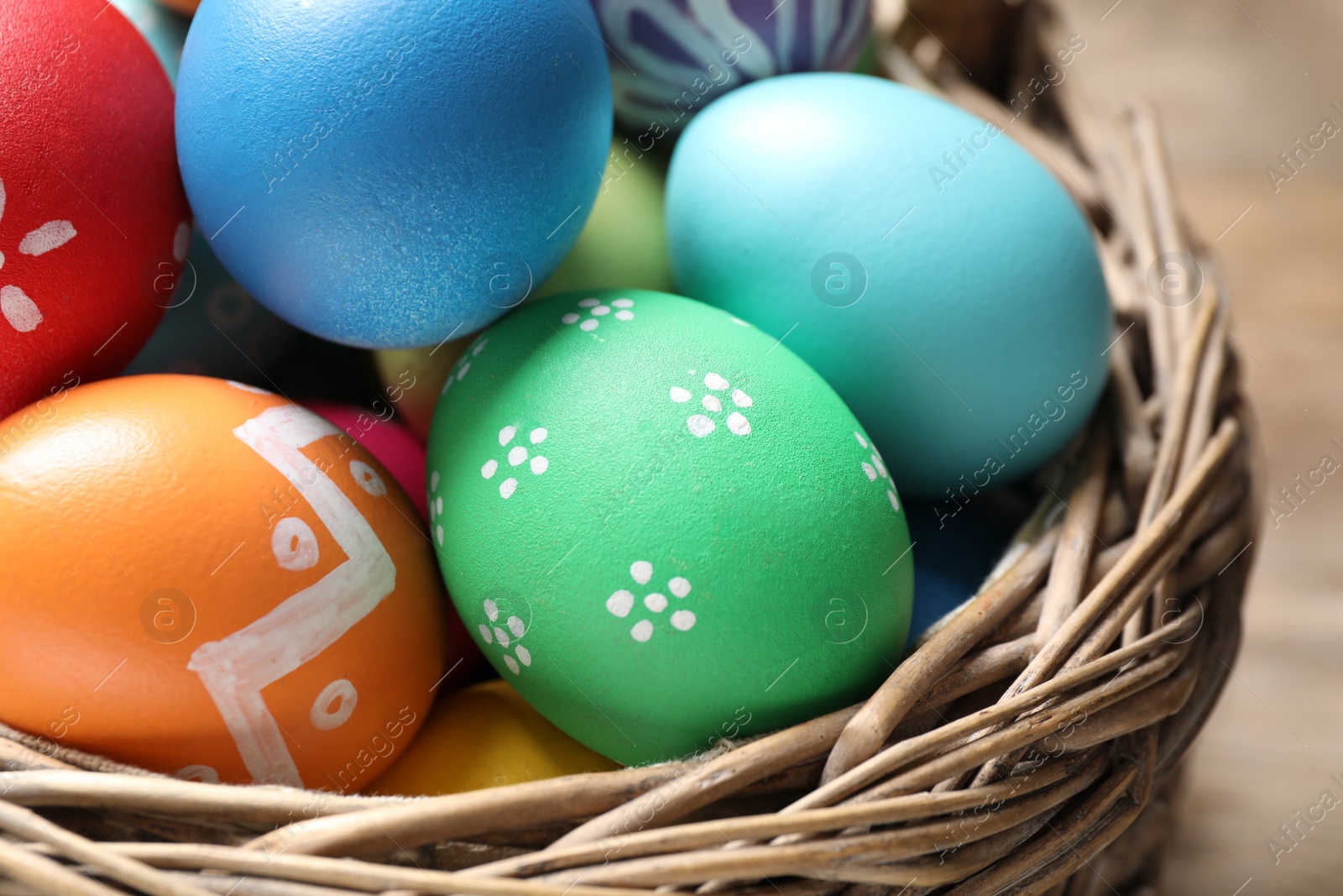 Photo of Basket with colorful Easter eggs on table, closeup