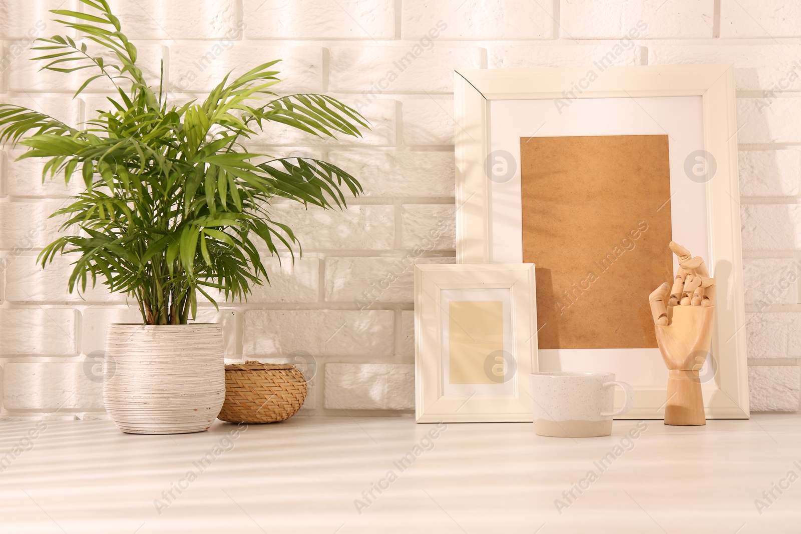 Photo of Stylish office workplace. Decor elements, plant and cup on white table near brick wall