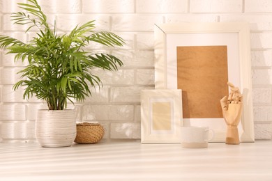 Photo of Stylish office workplace. Decor elements, plant and cup on white table near brick wall