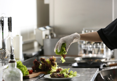 Photo of Female chef cooking tasty salad in restaurant kitchen, closeup