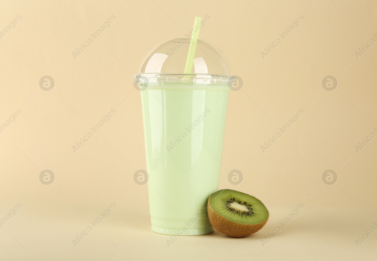 Photo of Plastic cup of tasty smoothie and fresh kiwi on beige background