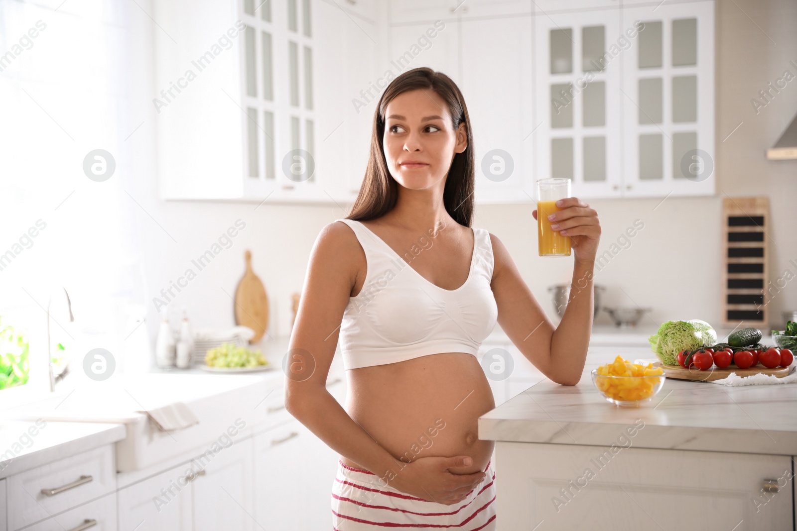 Photo of Young pregnant woman with glass of juice in kitchen. Taking care of baby health