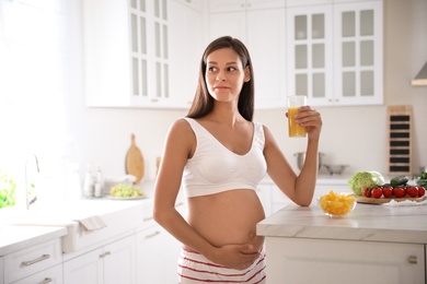 Young pregnant woman with glass of juice in kitchen. Taking care of baby health