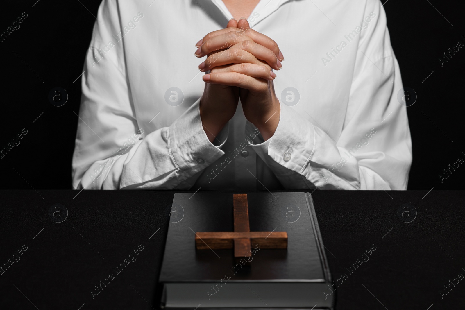 Photo of Woman holding hands clasped while praying at table with Bible and cross, closeup