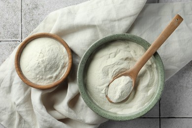 Photo of Bowls and spoon of agar-agar powder on tiled table, flat lay