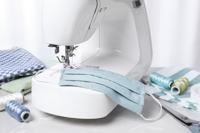 Photo of Sewing machine, homemade protective mask and craft accessories on grey table