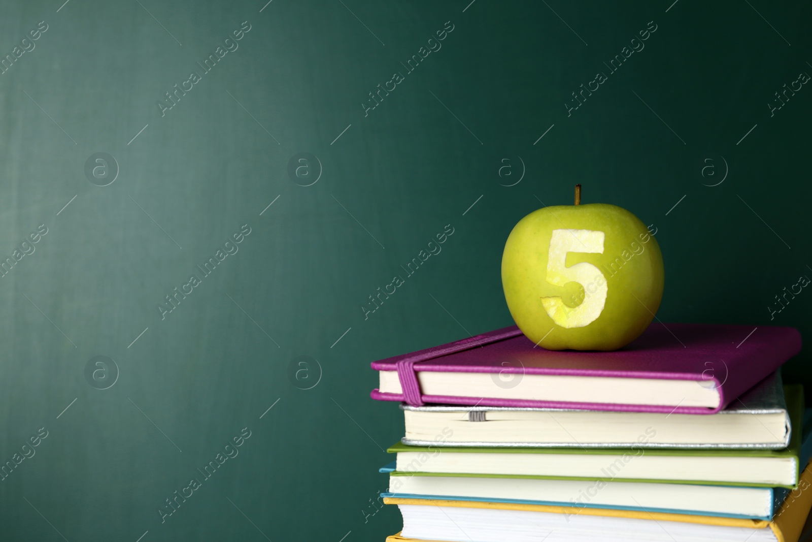 Image of Apple with carved number five as school grade on books near green chalkboard, space for text