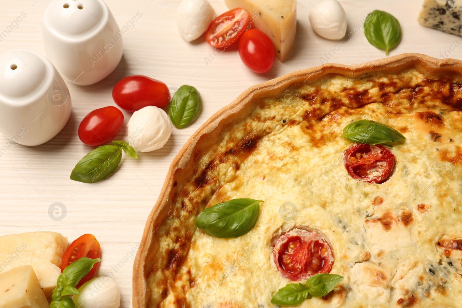 Photo of Delicious homemade cheese quiche and ingredients on wooden table