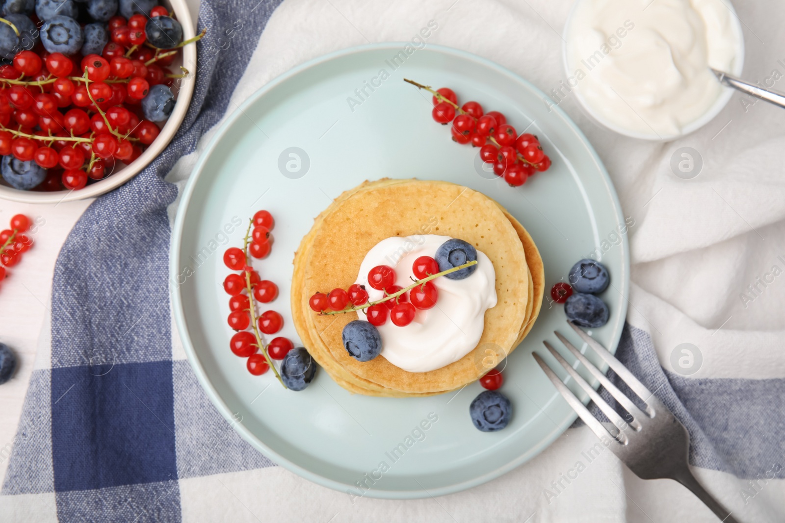 Photo of Tasty pancakes with natural yogurt, blueberries and red currants on table, flat lay