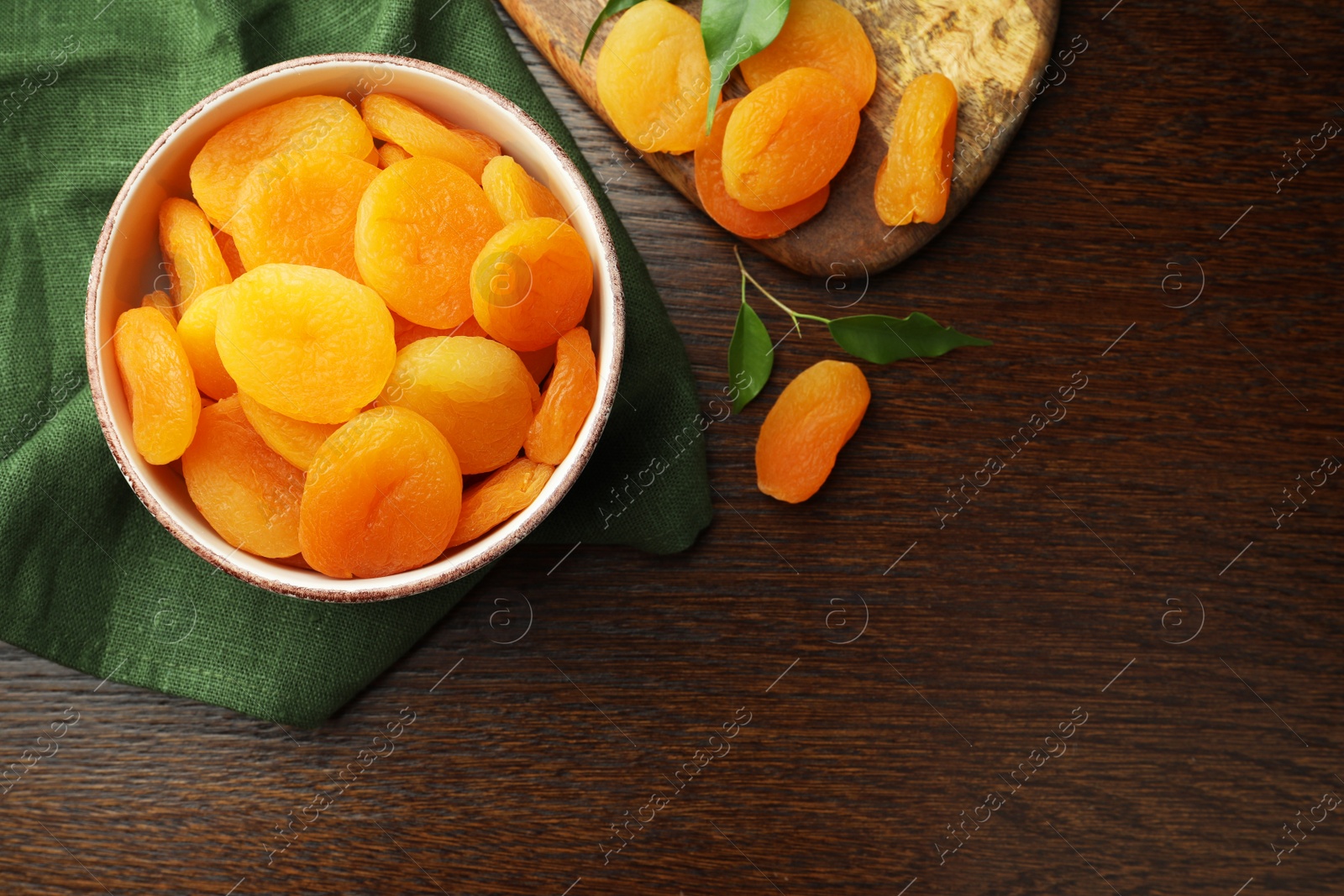 Photo of Tasty apricots with green leaves and space for text on wooden table, flat lay. Dried fruits