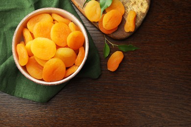 Tasty apricots with green leaves and space for text on wooden table, flat lay. Dried fruits