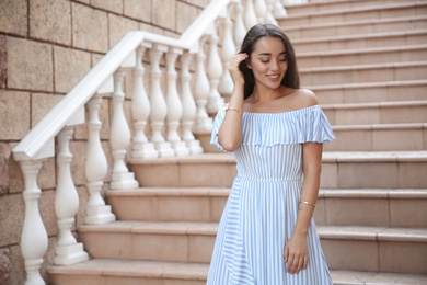 Photo of Beautiful young woman in stylish light blue striped dress on stairs outdoors