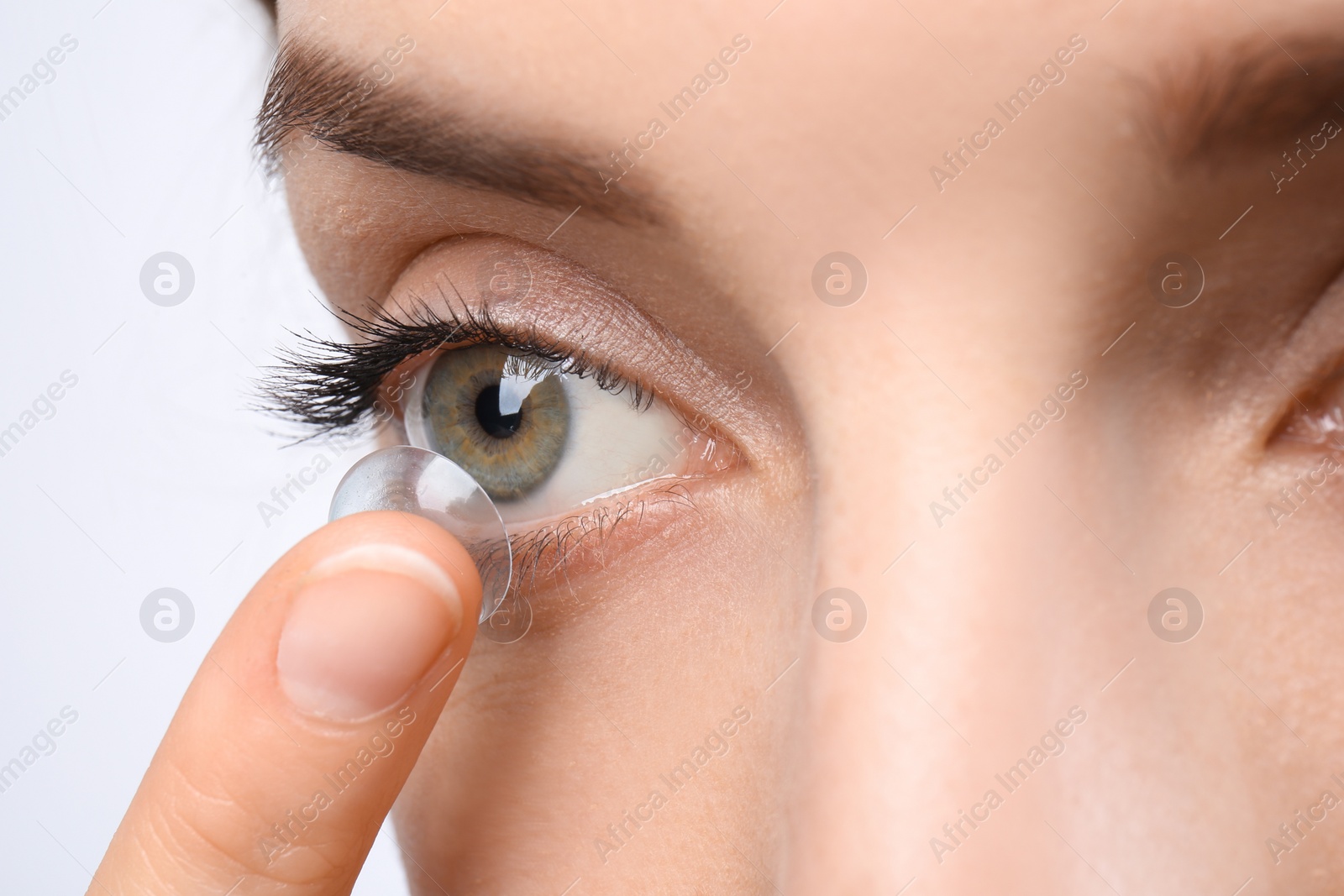 Photo of Young woman putting contact lens in her eye, closeup