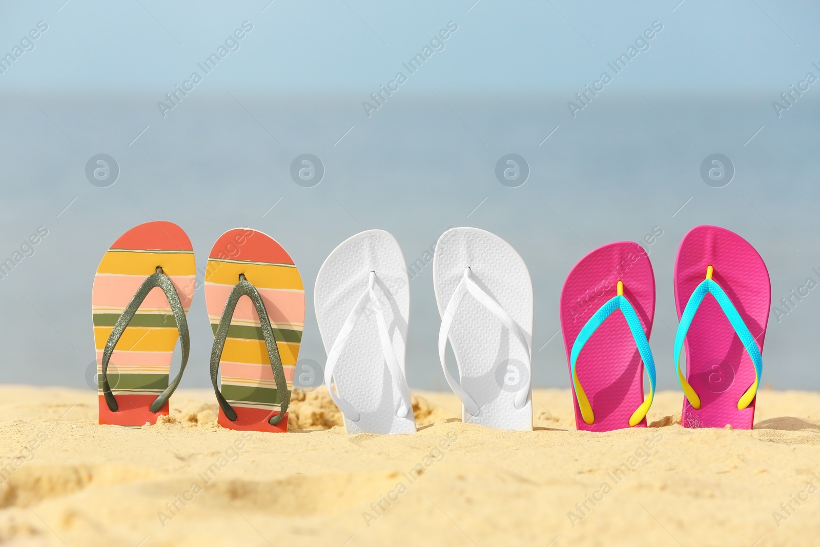 Photo of Different bright flip flops in sand. Beach accessories