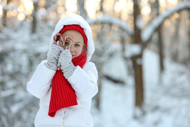 Photo of Cute little girl with candy canes in winter park, space for text