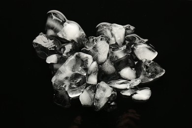 Photo of Pieces of crushed ice on black mirror surface, top view