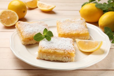 Tasty lemon bars with powdered sugar and mint on wooden table, closeup