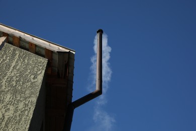 Photo of Metal chimney pipe with smoke against blue sky, low angle view