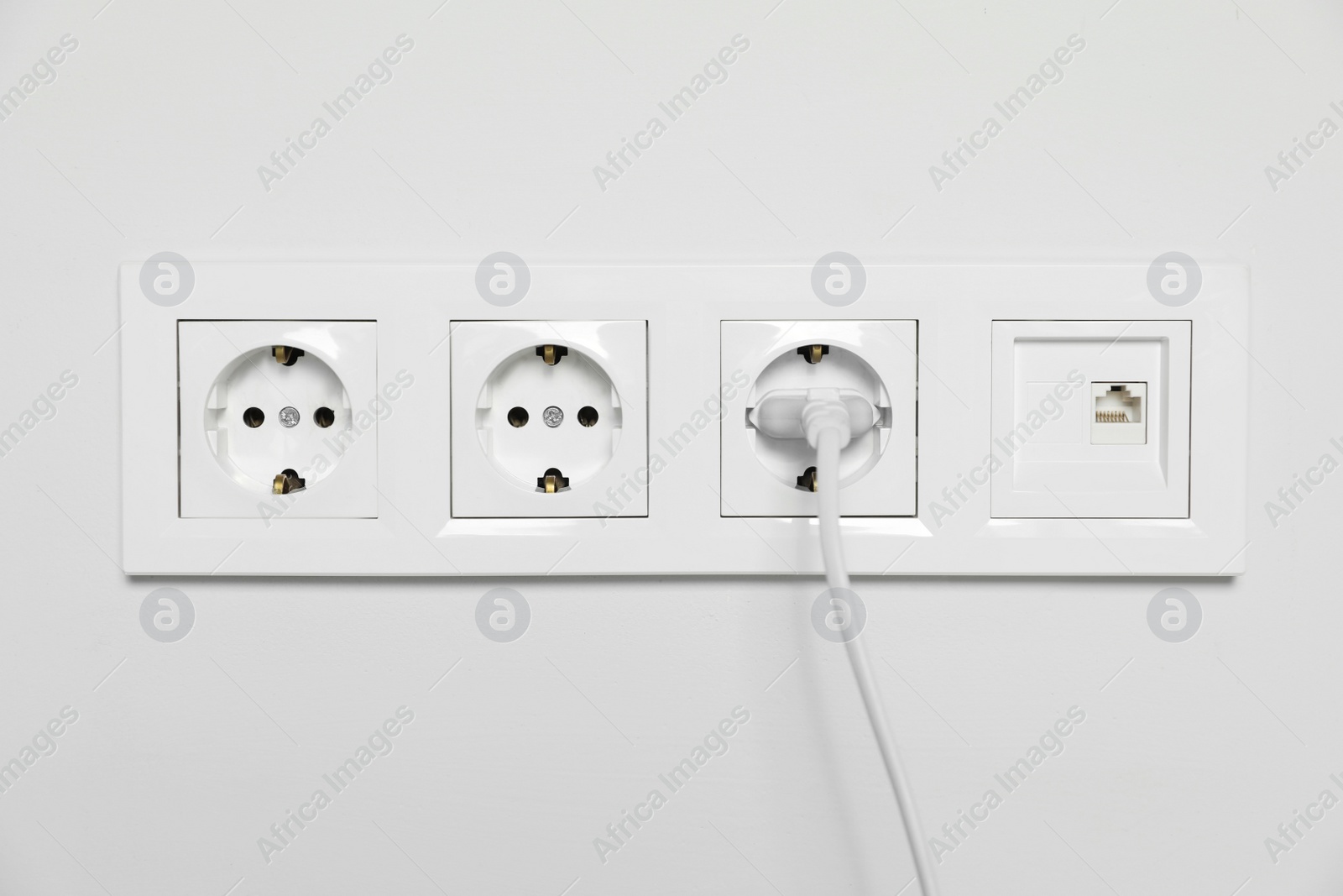 Photo of Power sockets with inserted plug on white wall. Electrical supply