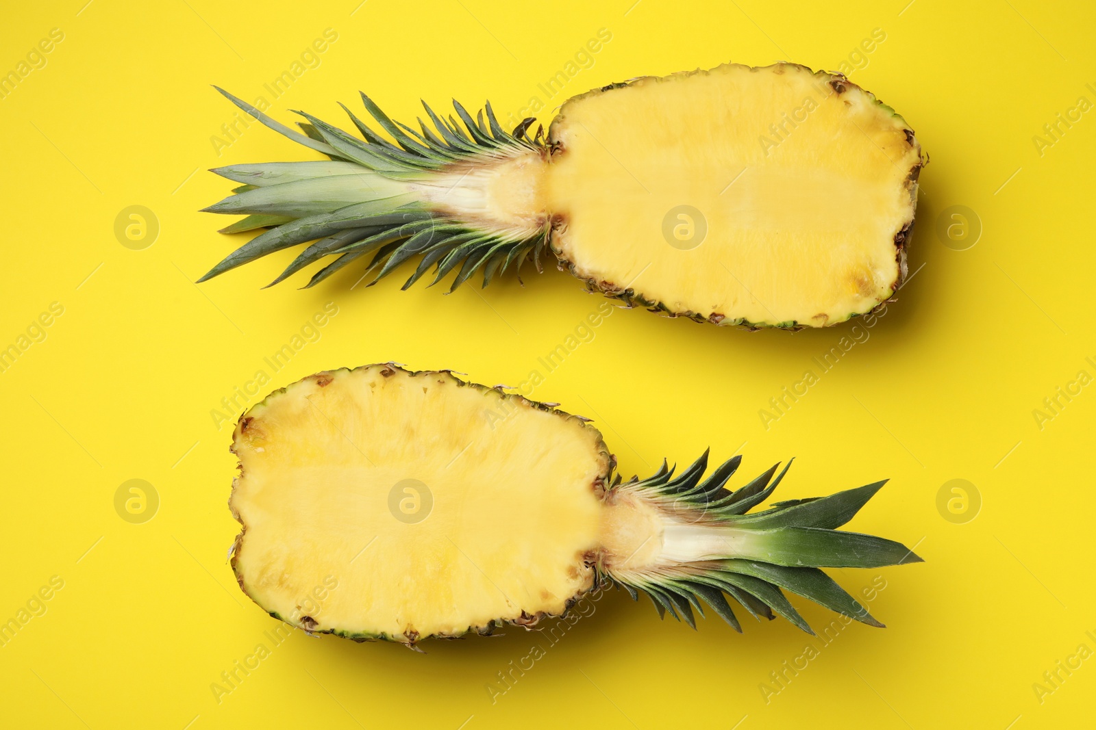 Photo of Halves of fresh pineapple on yellow background, top view