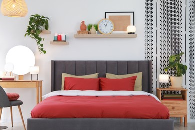 Photo of Stylish bedroom interior with comfortable bed, dressing table, lamps and green houseplants