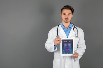 Photo of Male doctor holding tablet with urinary system on screen against grey background