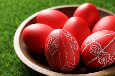 Photo of Wooden bowl with red painted Easter eggs on green grass, closeup