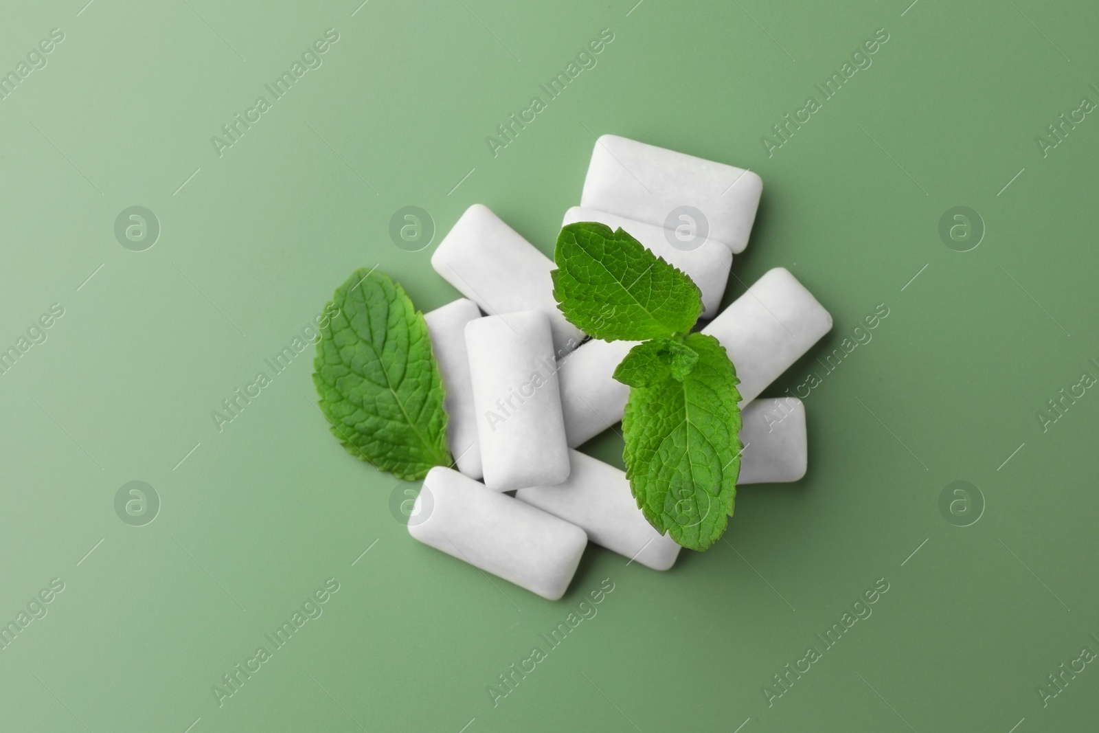 Photo of Tasty white chewing gums and mint leaves on light green background, top view