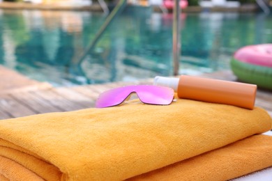 Beach towels, sunglasses and sunscreen on sun lounger near outdoor swimming pool, closeup. Luxury resort