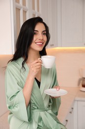 Pretty young woman wearing beautiful silk robe with cup of coffee in kitchen