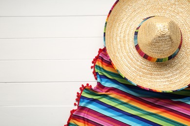 Photo of Mexican sombrero hat and colorful poncho on white wooden background, flat lay. Space for text