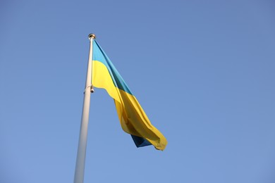 Flag of Ukraine fluttering against blue sky, low angle view. Space for text