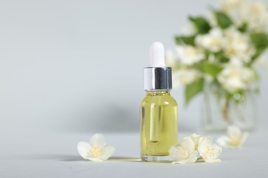 Photo of Essential oil in bottle and beautiful jasmine flowers on grey background, closeup. Space for text