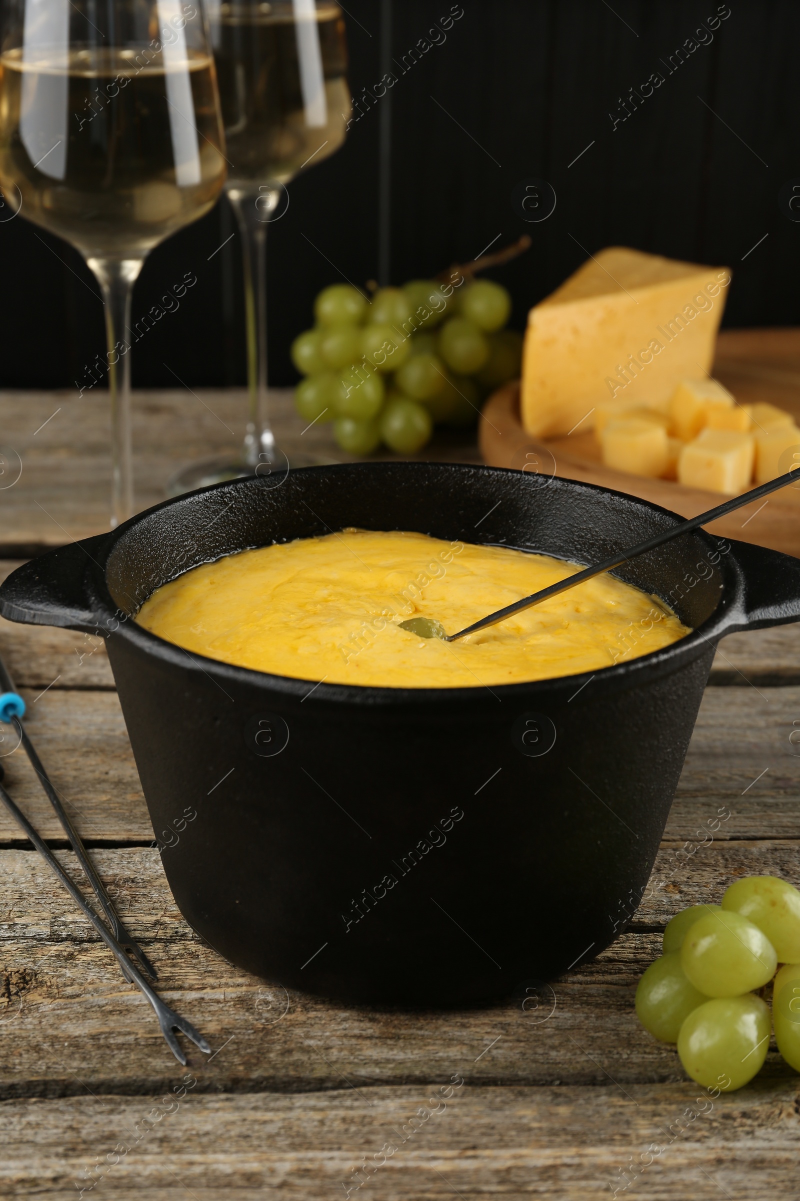 Photo of Fondue pot with melted cheese, glasses of wine and different products on wooden table