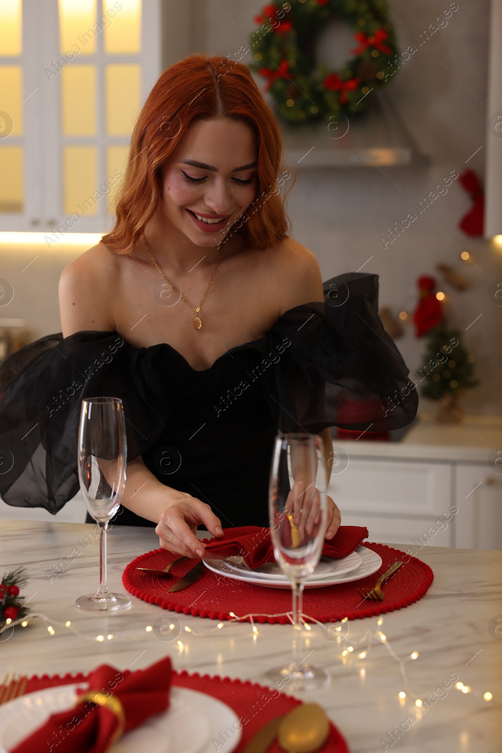 Photo of Beautiful young woman setting table for Christmas celebration in kitchen