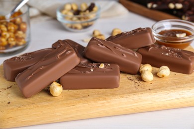 Photo of Delicious chocolate candy bars with nuts on white wooden table, closeup
