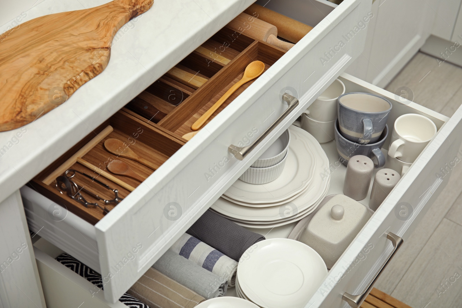 Photo of Open drawers of kitchen cabinet with different dishware, utensils and towels