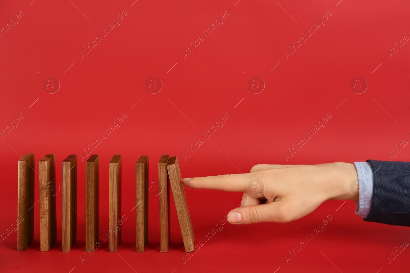 Photo of Woman causing chain reaction by pushing domino tile on red background, closeup. Space for text