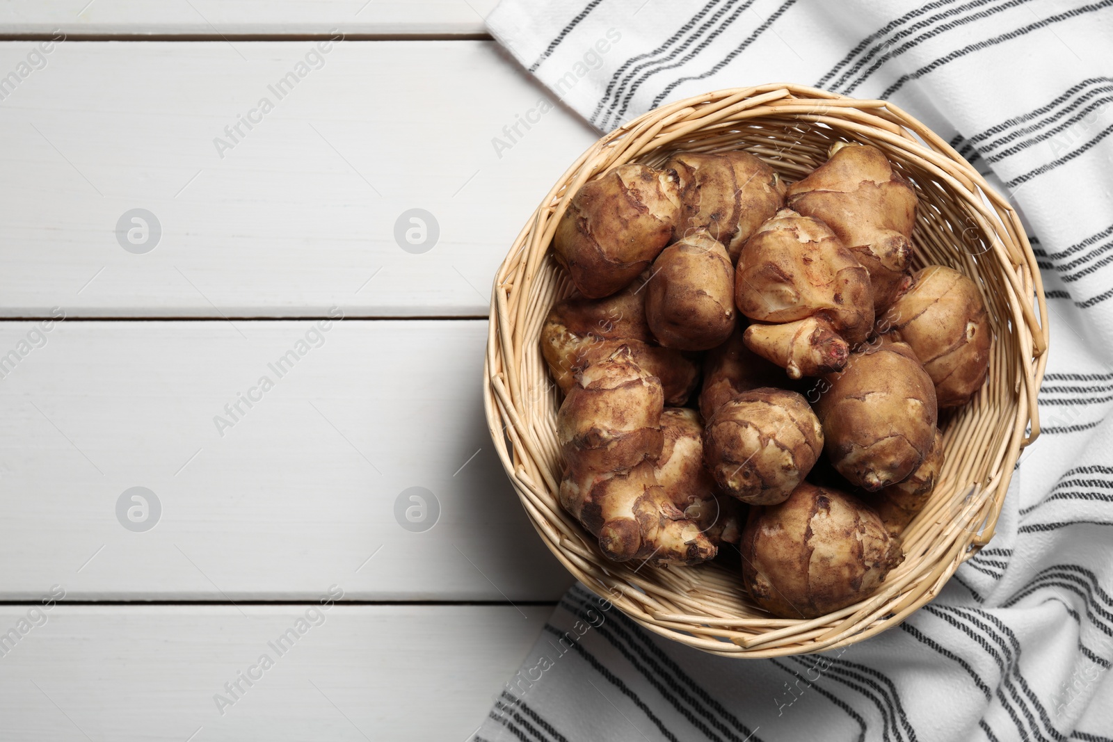 Photo of Wicker basket with fresh Jerusalem artichokes on white wooden table, top view. Space for text