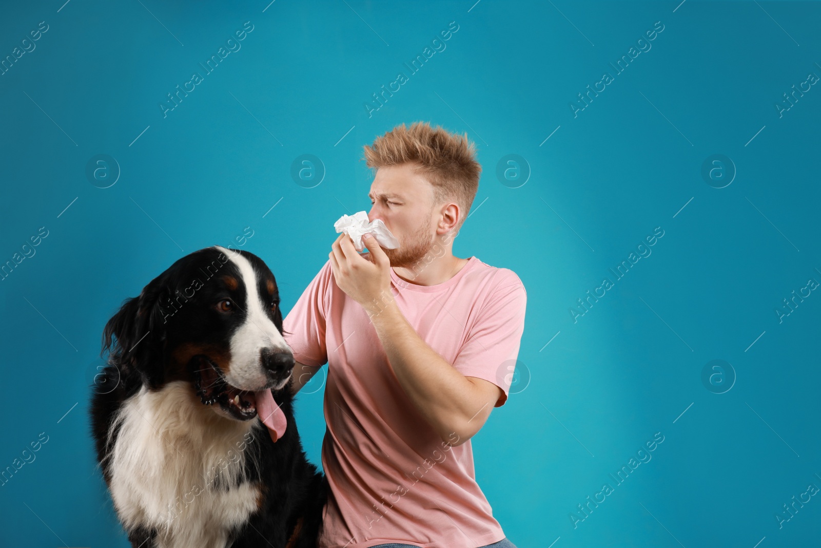 Photo of Young man suffering from fur allergy on blue background