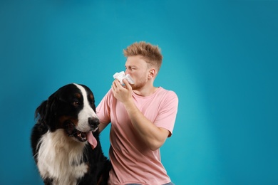 Photo of Young man suffering from fur allergy on blue background